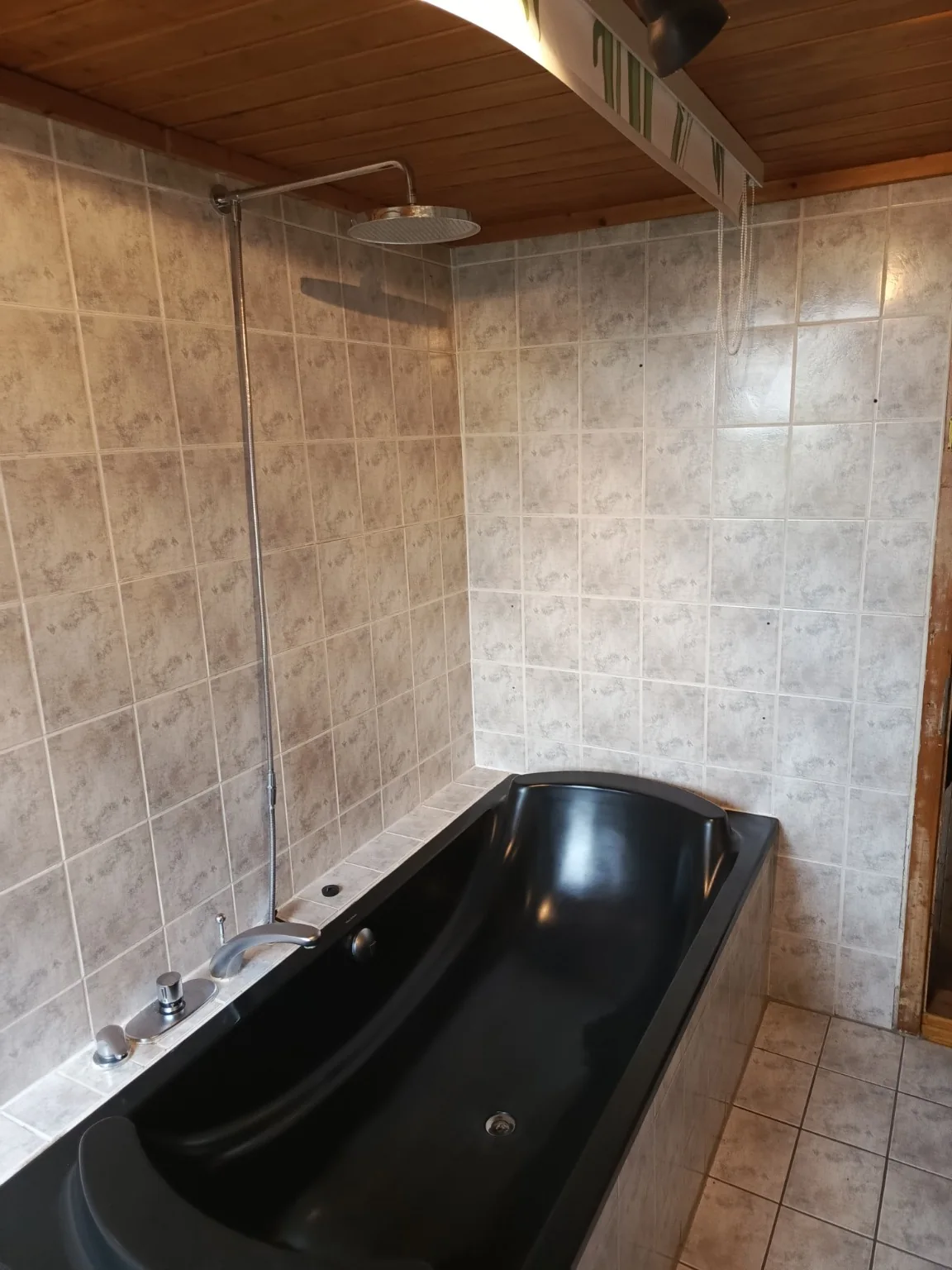 Vorher: Hohe schwarze Badewanne in einem gefliesten Badezimmer.